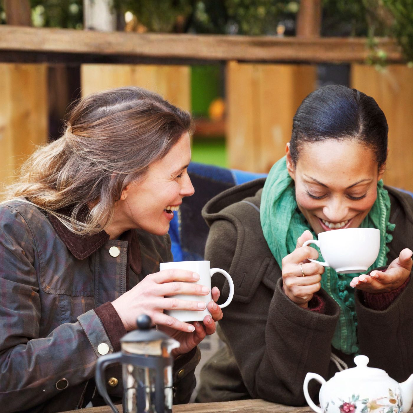 Two women sharing warm drinks in Miracle Manor, reflecting the ease and balance of friendships formed after 40.
