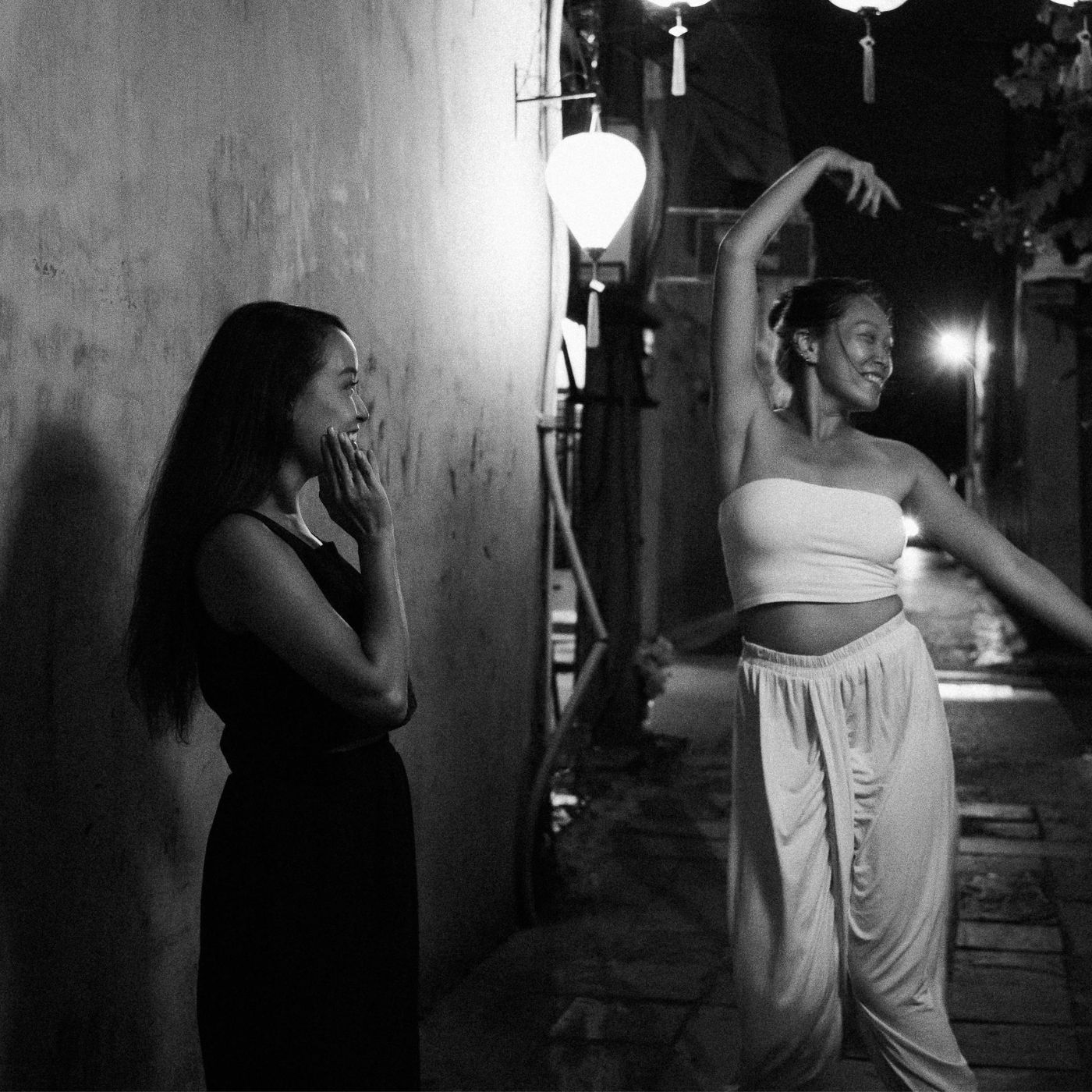 Two women smiling and interacting under street lights in a Kern alley