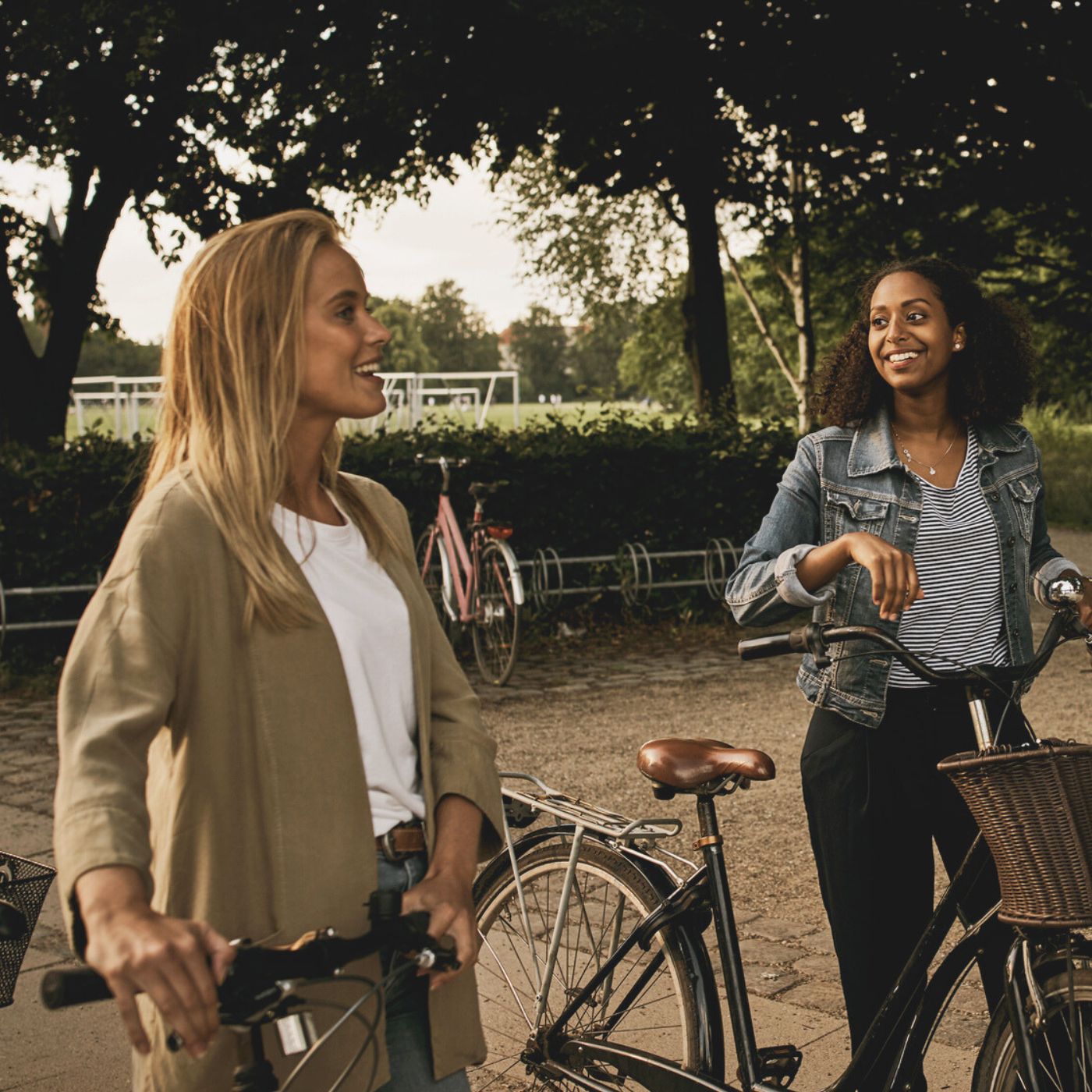 Two women with bicycles smiling and chatting in a Sacramento park setting