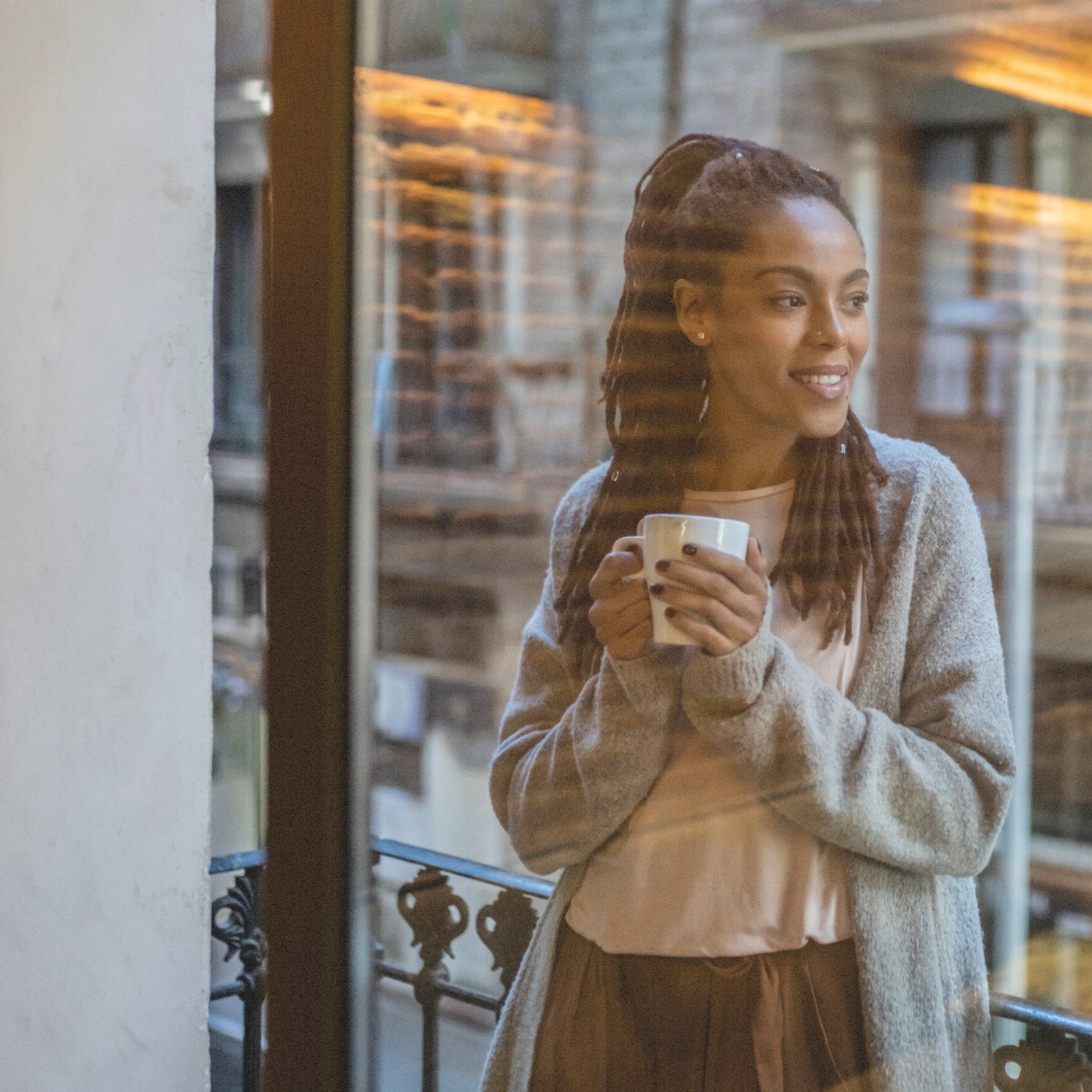 Woman gazing thoughtfully outside with warm drink in White Knoll, reflecting in new surroundings