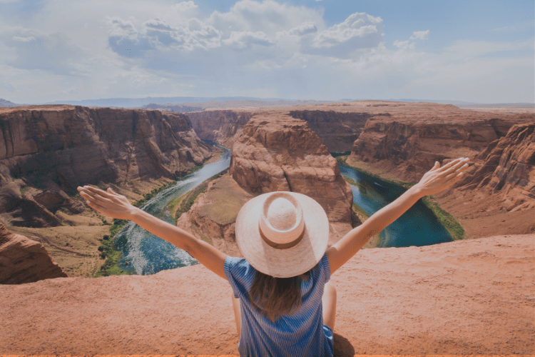 A woman with open arms sits at the edge of a vast canyon, celebrating freedom, joy, and the power of friendship in the open air