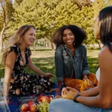 Labor Day activities with friends: three women enjoying a picnic together in a sunny park.
