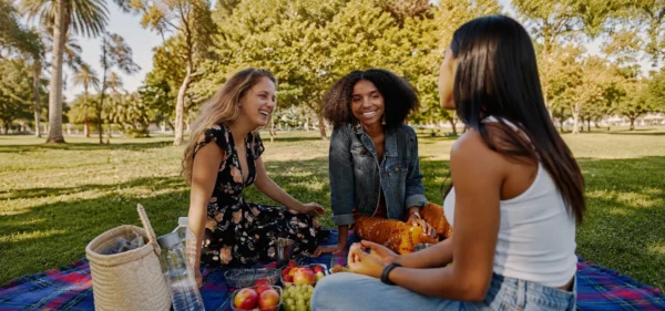 Labor Day activities with friends: three women enjoying a picnic together in a sunny park.