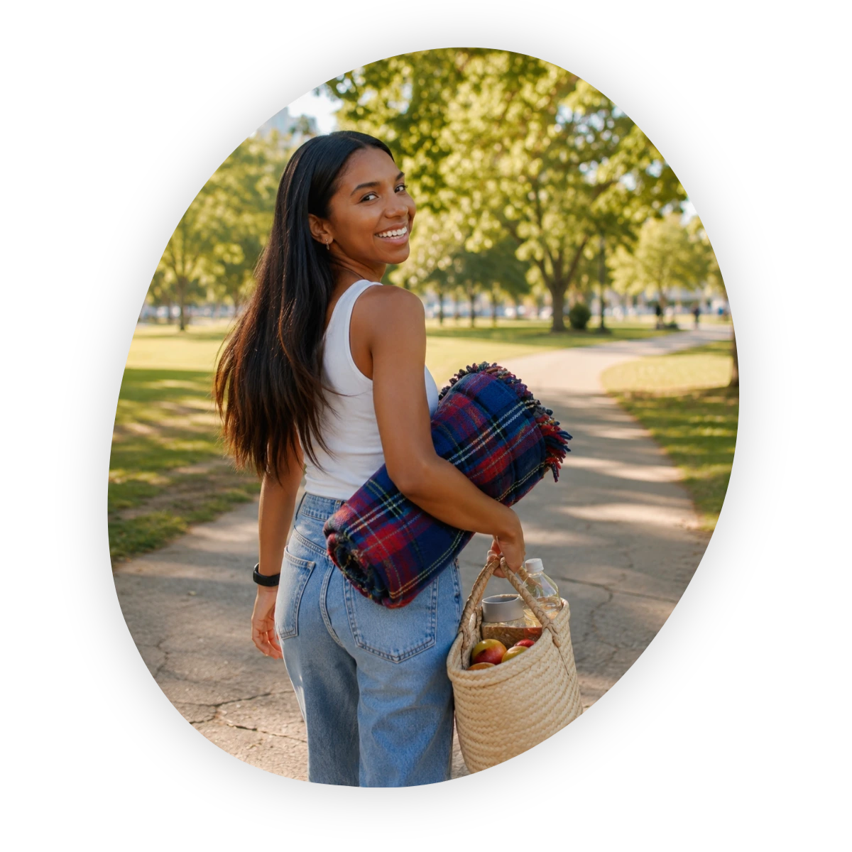 Labor Day activities with friends: woman carrying a picnic basket and blanket through a sunny park.